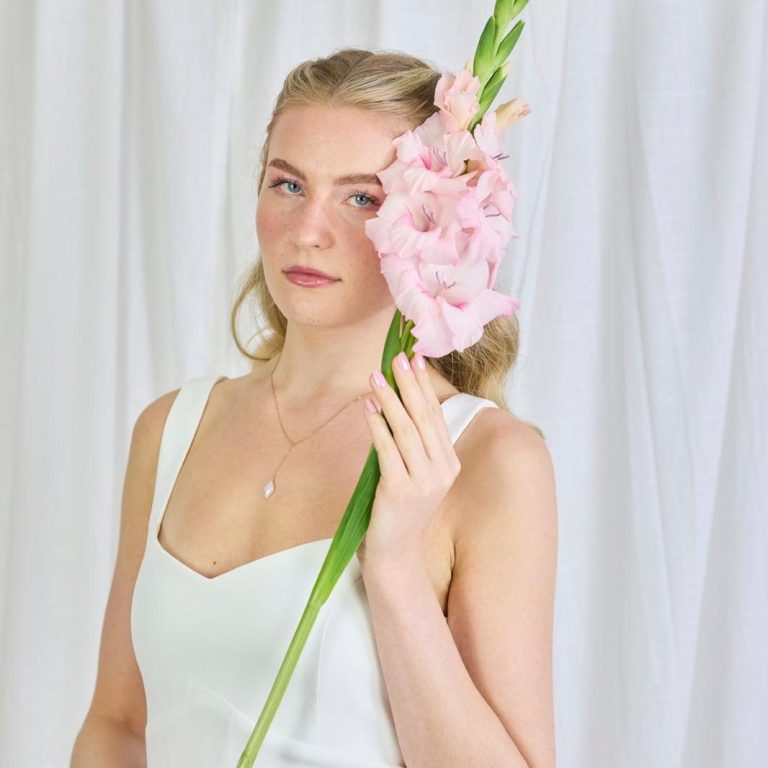 Dein Brautoutfit für deine einzigartige Strandhochzeit. Braut am Ostseestrand bei einer Strandhochzeit. Ein Oberteil mit pastellfarbigen Blumen und einen Brautstrauß in der Hand.