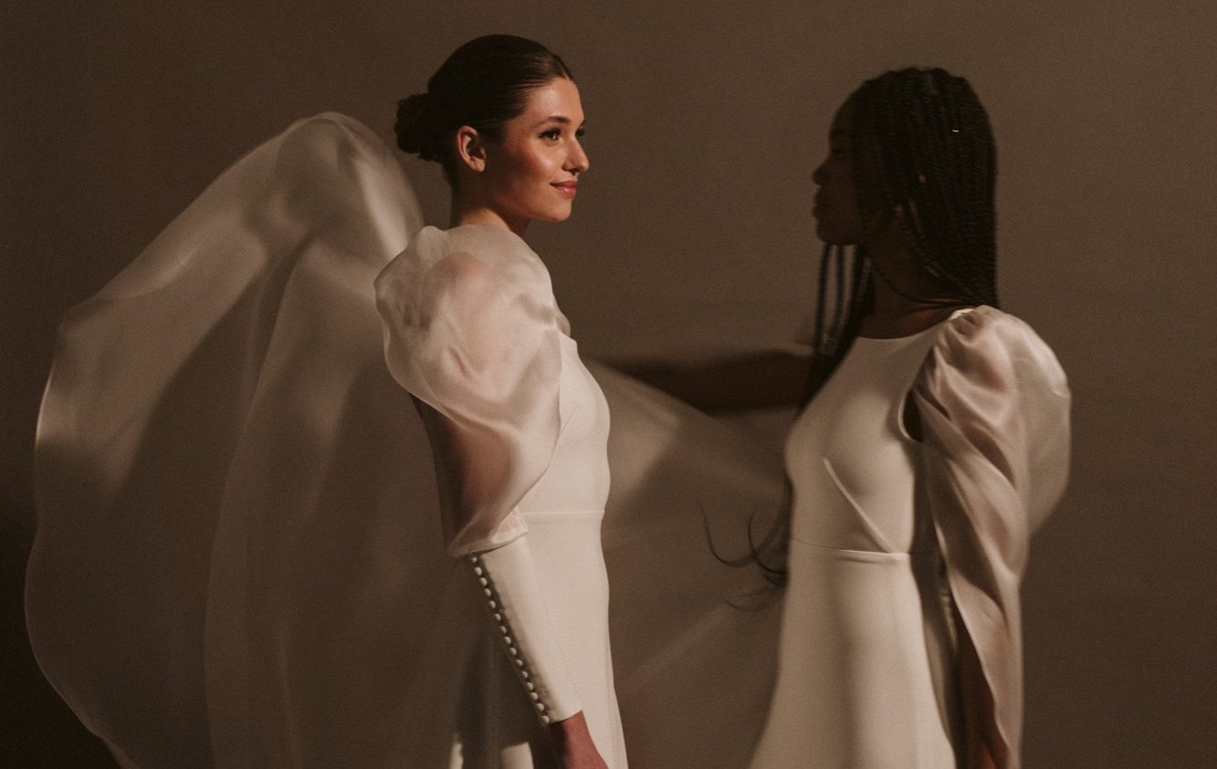 Hochzeit am Strand mit einem Zweiteiler und langem Schleier. Braut steht am Strand vor der Wasserkante und ein Schleier weht vor ihr im Wind.