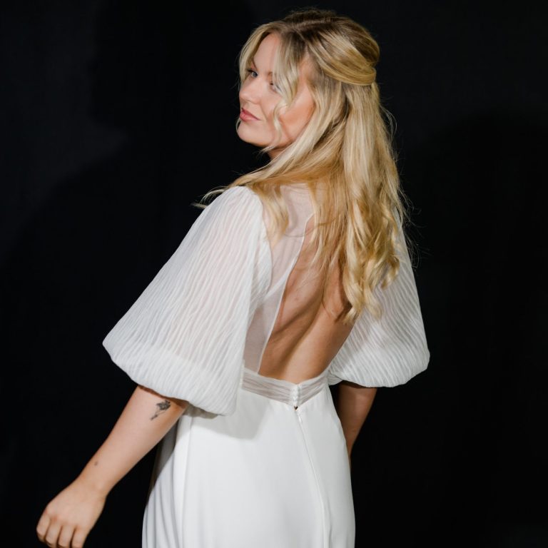 Lockerer Stoff für dein Brautkleid - Perfekt für die Gartenparty. Brautkleid wird von hinten gezeigt vor einem schwarzen Hintergrund. Das Kleid hat Puffärmel aus hochwertigem Organza.